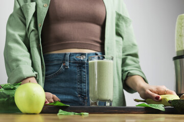 Unrecognizable woman in casual wear with glass of fresh blended healthy green vegan smoothie....