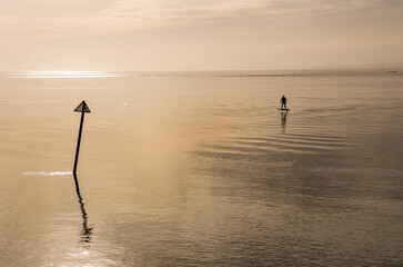 Man on a Electric surfboard rides in a calm and relaxing seascape with reflective still waters in...