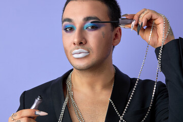 transvestite man applying ink on eyelashes, isolated over purple background, isolated over purple...