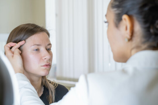 Doctor assesses young woman's complexion, emphasizing attentive healthcare. Connects with proactive skin treatment.