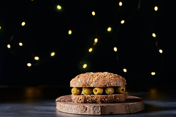 Bread bun filled with salad and olives on a dark background.