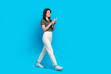 Fototapeta na wymiar Full length profile photo of gorgeous positive person use smart phone walk empty space isolated on blue color background