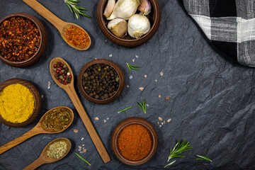 Spices and condiments in wooden utensils on black stone background. Free space for text.
