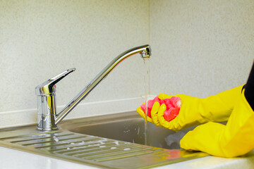 woman wets a sponge while cleaning the kitchen.