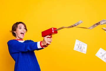 Photo of cool cheerful lady dressed knitted sweater shooting money gun isolated yellow color background