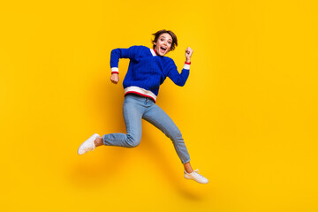 Full length photo of funny lucky lady dressed knitted sweater rising fists jumping high empty space isolated yellow color background