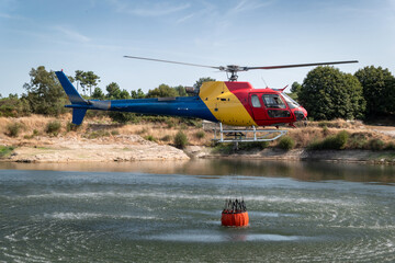 Operação aérea de combate: Helicóptero bombeiro recarrega o seu balde suspenso em lago durante...
