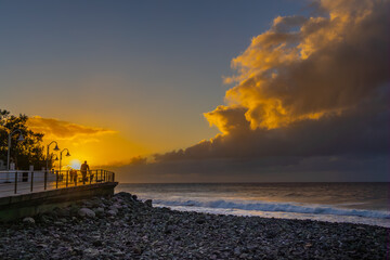 Sea and boardwalk with silhouettes of people in sunset at Puerto de las Nieves, Agaete, Gran Canaria, Spain.