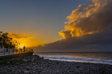 Sea and boardwalk with silhouettes of people in sunset at Puerto de las Nieves, Agaete, Gran...