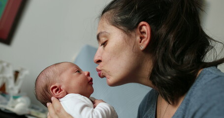 Mother and newborn baby interaction mom kissing infant during first day of life showing love and affection