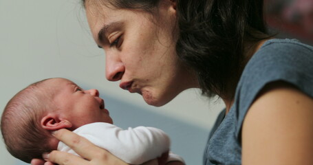 Mother and newborn baby interaction mom kissing infant during first day of life showing love and affection