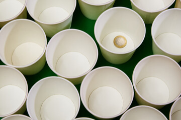 White empty paper cups, one of which contains a 1 euro coin. Leave a donation, give alms, play the lottery