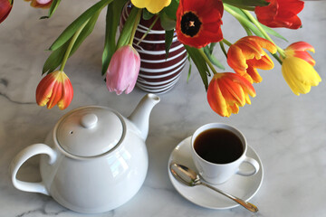 Early spring morning background - teapot and cup of tea by colorful vase of tulips flowers