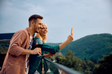 Happy couple taking selfie with smart phone on terrace.