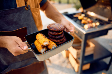 Close up of man with grilled corn and hamburgers.