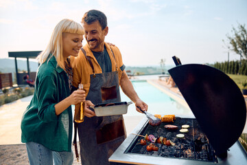 Happy couple grilling food on barbecue at poolside.