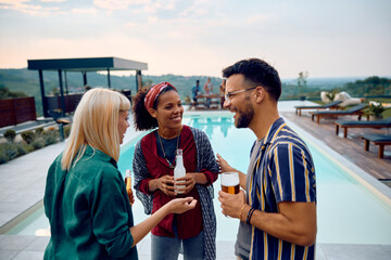 Cheerful friends talking while having drink at pool party.