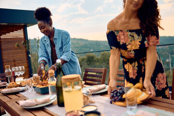 Happy black woman setting dining table on terrace.