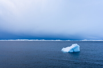 cold iceberg in polar regions in the ocean, with snowy mountains on the horizon