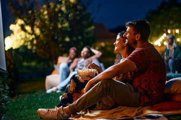 Happy couple relaxing during movie night with friends in backyard.