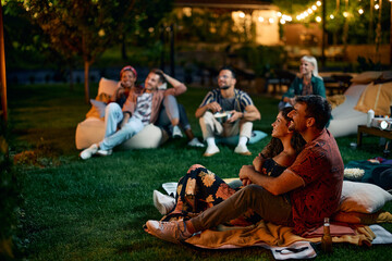 Embraced couple watching movie with friends in backyard.