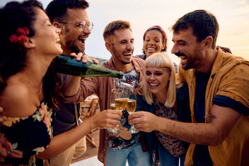 Cheerful friends having fun while toasting with champagne on outdoor party.