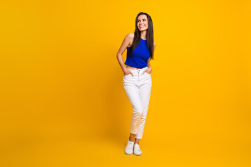 Fototapeta na wymiar Full length photo of cheerful cute woman wear blue top looking empty space isolated yellow color background