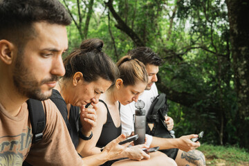 group of woman and man looking at cellphones in while sitting in forest