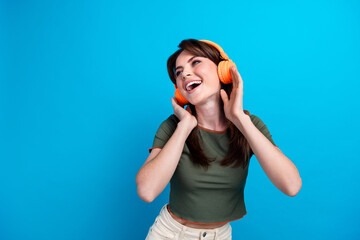 Photo of lovely positive girl hands touch headphones look empty space ad isolated on blue color...