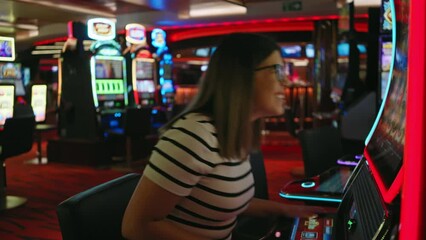 A joyful woman plays a slot machine in a lively casino, exuding excitement and entertainment.