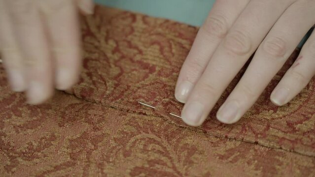 This video shows a hand sticking sewing needles in upholstery fabric hemline. 