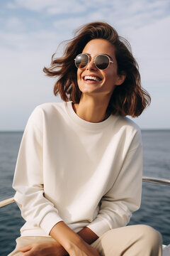 Sweatshirt mockup one woman wearing blank white crewneck smiling on a boat at sea wearing sunglasses 