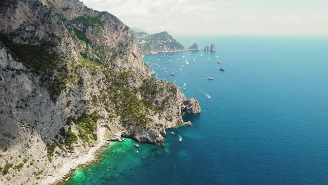 Capri's Limestone Cliffs Tower Over Tranquil Sea. The rugged coastline forms a stark contrast with the gentle marine activities below. Italian summer holidays.