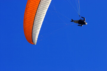 a paraglider with an orange and white canopy in the blue sky