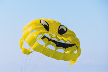 Yellow parachute with smiley face on sky background. Flying parachute with a smiley face