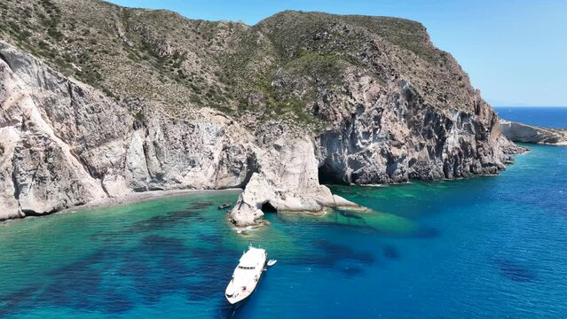 Aerial drone video of beautiful turquoise beach and cave formations visited by yachts and sailboats in Southern part of Antiparos island, Cyclades, Greece