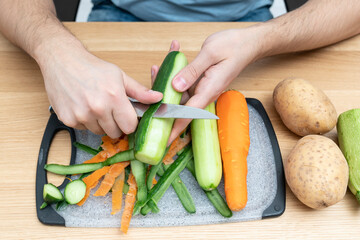 Close-up shot of a man peeling vegetables using special vegetable peelers in the kitchen