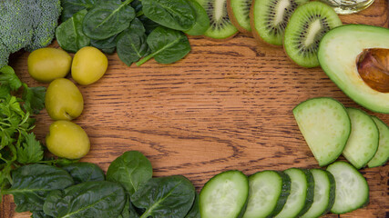 a wooden table with a variety of green fruits and green vegetables. Copy space.