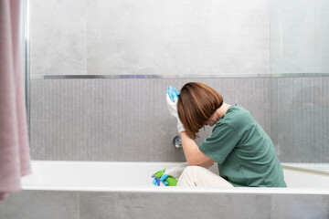 A tired girl cleans the bathtub with a rag in the bathroom. Household and cleaning concept
