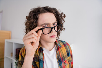 Photo of suspicious unsure guy dressed checkered shirt arm eyewear suspiciously looking you indoors...