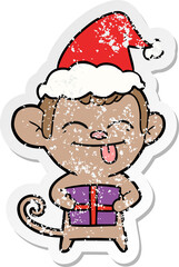 funny distressed sticker cartoon of a monkey with christmas present wearing santa hat