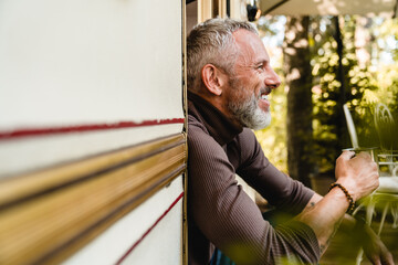 Close up side view portrait of a senior handsome man with cheerful smile and a mug of tea sitting...