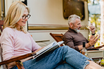 Close up portrait of mature blonde woman wearing glasses while reading near her husband and their...