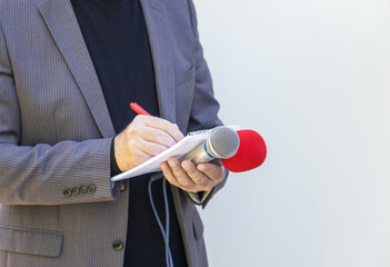 Reporter or journalist at media event, holding microphone, writing notes. Journalism concept with...