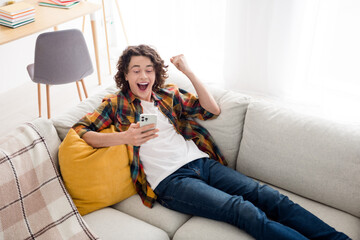 Photo of cheerful lucky guy wear plaid shirt lying sofa winning gale modern gadget indoors room home house