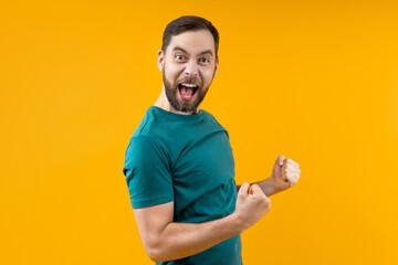 Portrait of joyful young man with wide open mouth and clenched fists celebrating money win in online lottery or at bookmaker's, isolated over yellow background
