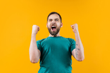 Joyful, excited, glad bearded man with wide open mouth and clenched fists celebrating money win in online lottery or at bookmaker's, isolated over yellow background - obrazy, fototapety, plakaty