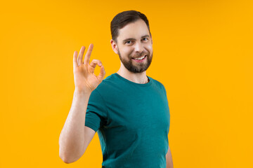 Studio shot of attracting smiling young man showing ok gesture, isolated over bright colored orange yellow background - 725861050