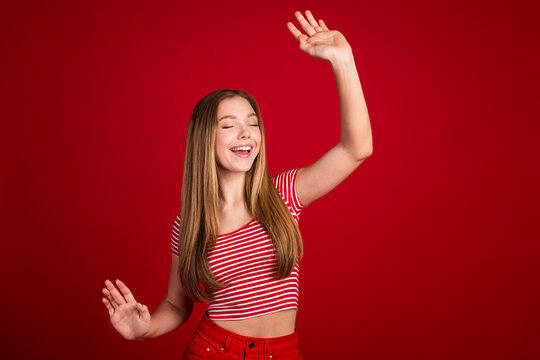 Photo of adorable lovely schoolgirl with straight hairdo dressed striped top dansing hand up eyes closed isolated on red color background