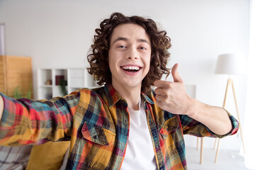 Photo of cheerful confident guy dressed checkered shirt showing thumb up tacking selfie indoors...